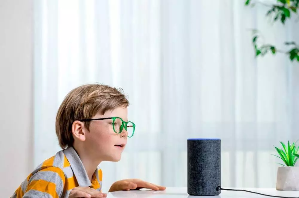 Mozrest - Young boy with green glasses speaking to a virtual assistant at home