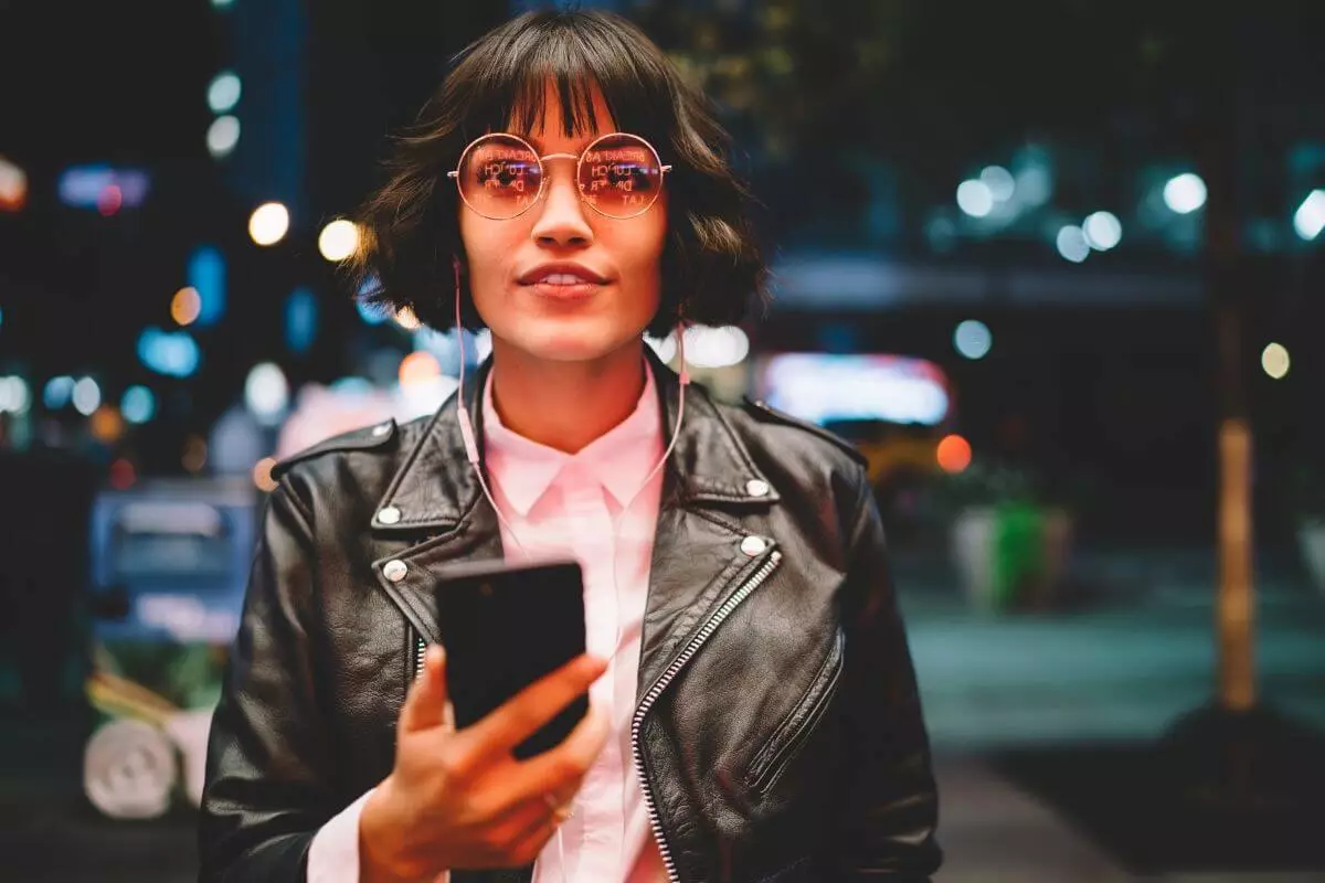 Mozrest - Smiling woman using her smartphone in a city street at night