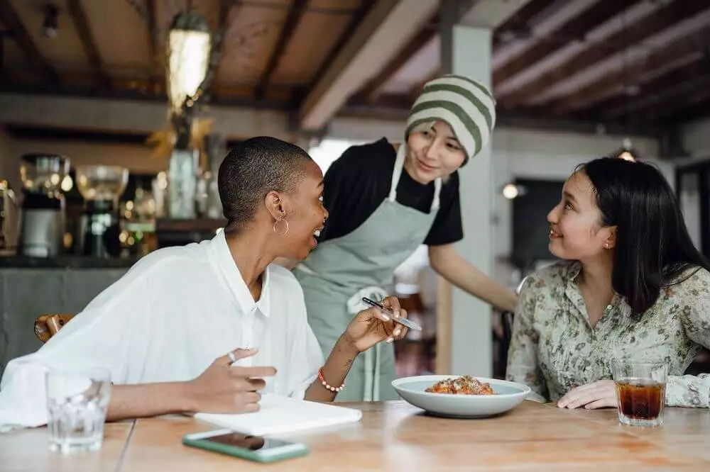 Mozrest - Two customers sitting at a table are asking a waiter for advice and recommendation about the food in a restaurant