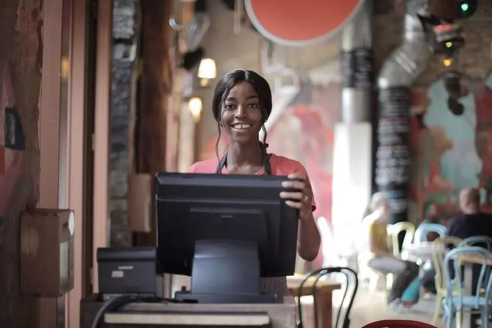 Mozrest - A smiling waitress is smiling at us behind her reservation and table management software in a restaurant.