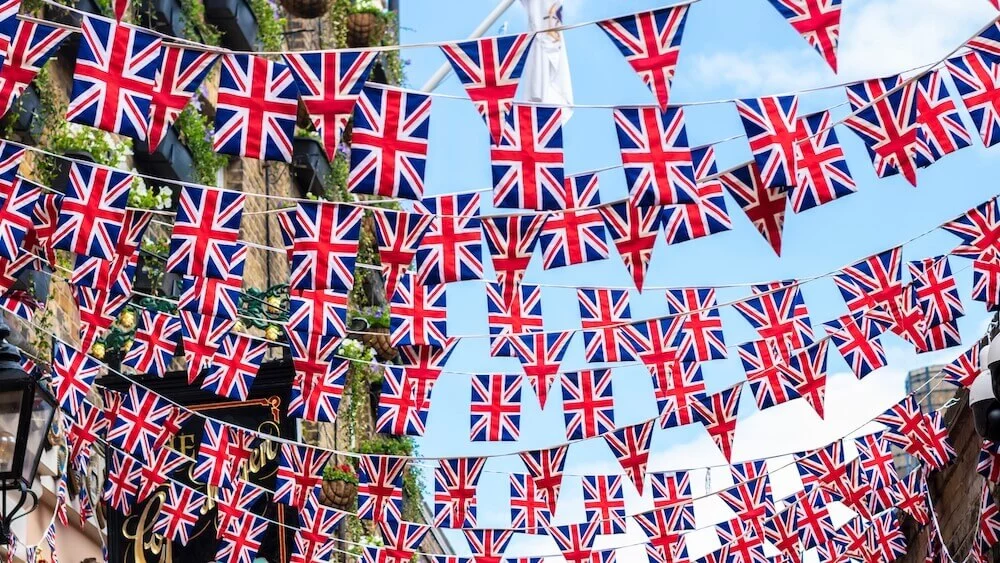 A street where stands a pub is decorated with multiple garlands of union jack flags to celebrate a special event during a Bank Holiday Weekend.