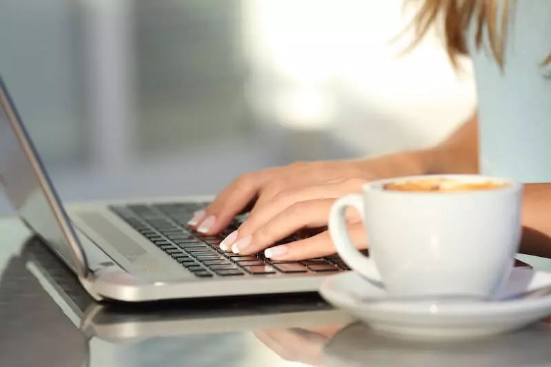 Femme assise à une table avec une tasse de café gérant facilement les profils et avis clients de son restaurant.