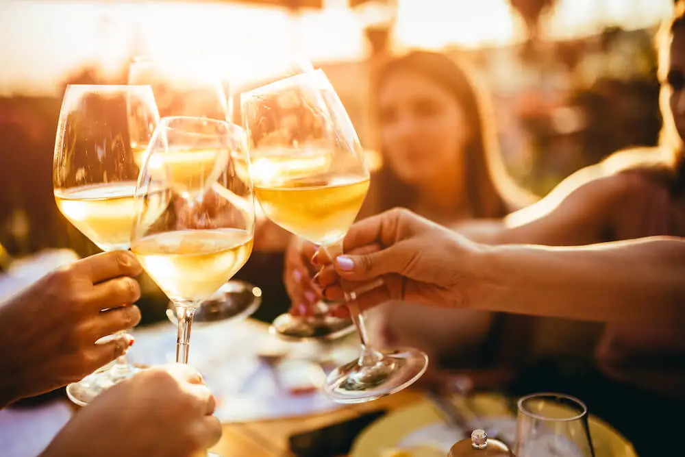 Mozrest - Group of friends cheering with white wine glasses on a restaurant's terrace during a Bank Holiday Weekend