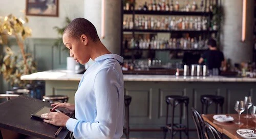 Mozrest - Solutions for Restaurant - Waitress looking at her tablet at the entrance of a restaurant checking the bookings for the day before welcoming guests