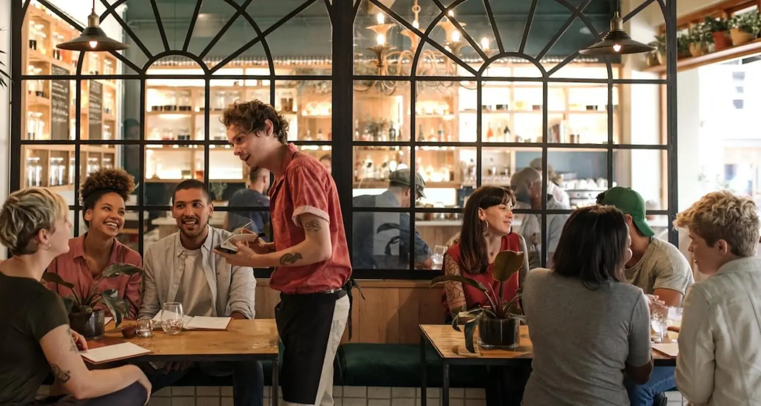 Mozrest - Lösungen für Restaurants - Kellner, der die Bestellung von lächelnden Gästen in einem geschäftigen Restaurant aufnimmt.