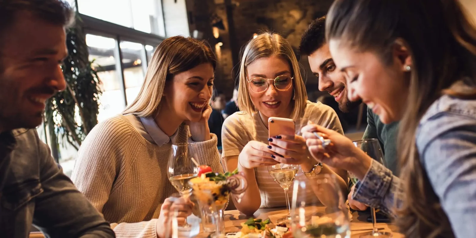 Mozrest - Solutions for Booking Channels - Group of friends seating at a table in a restaurant searching for a their next place to eat on their mobile phone