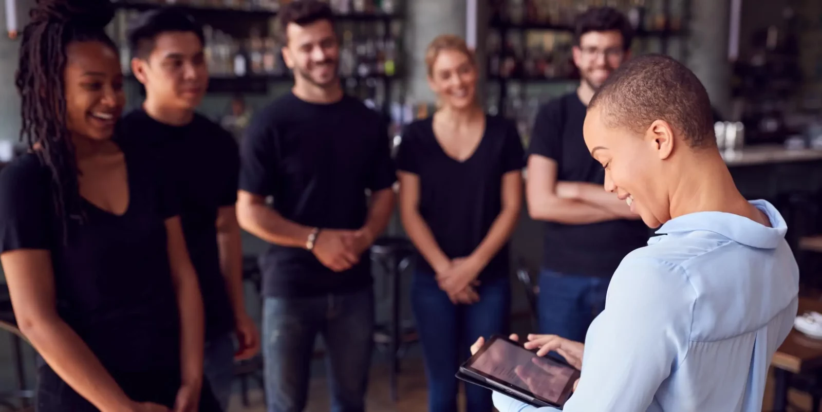 Mozrest - Solutions for Restaurant - Restaurant manager briefing her staff, smiling, and checking the number of today's bookings on her tablet