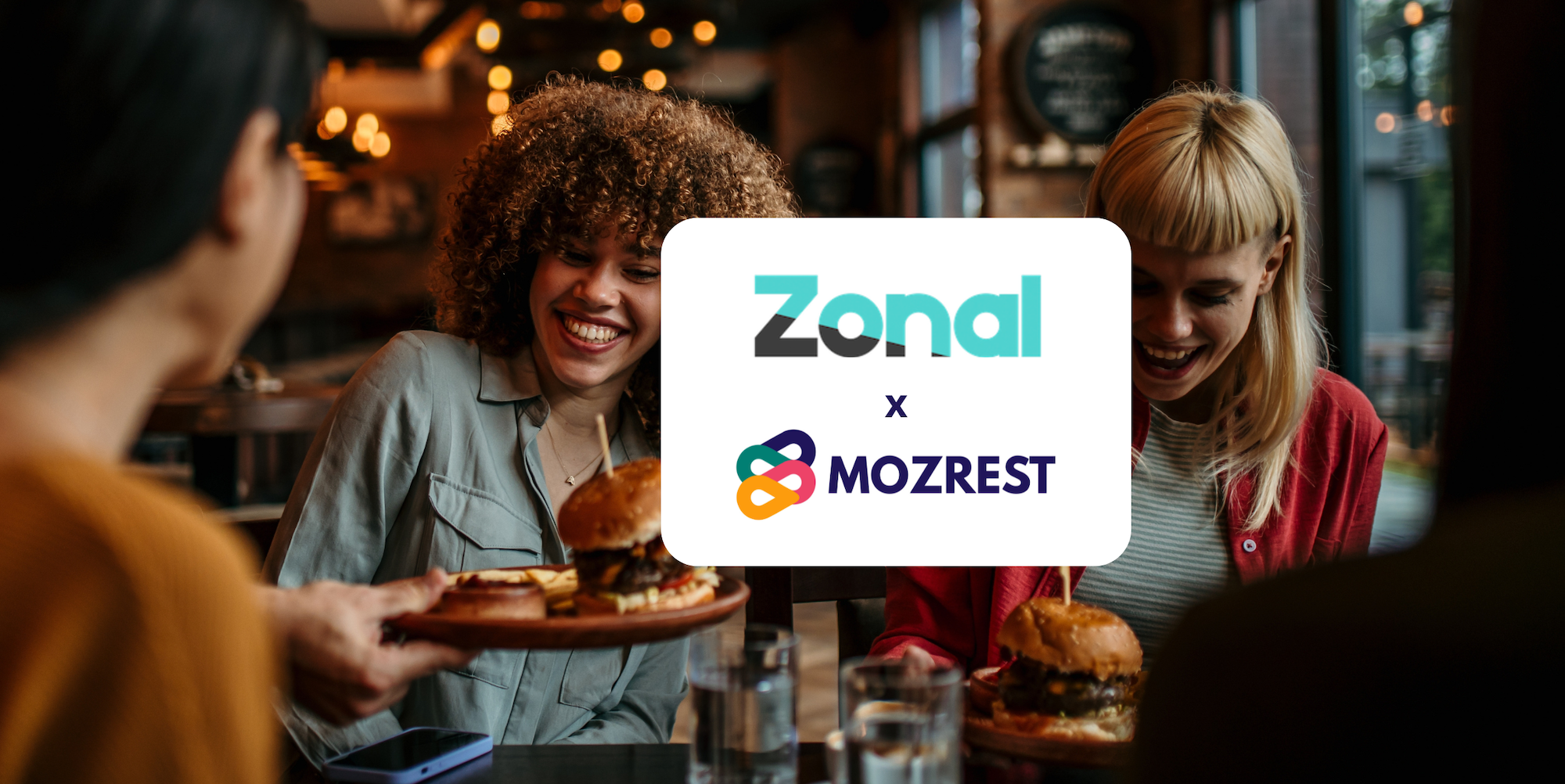Mozrest - Solutions pour les Canaux de Réservation - Un groupe d'amis assis à une table dans un restaurant cherchant leur prochain endroit où manger sur leur téléphone mobile.