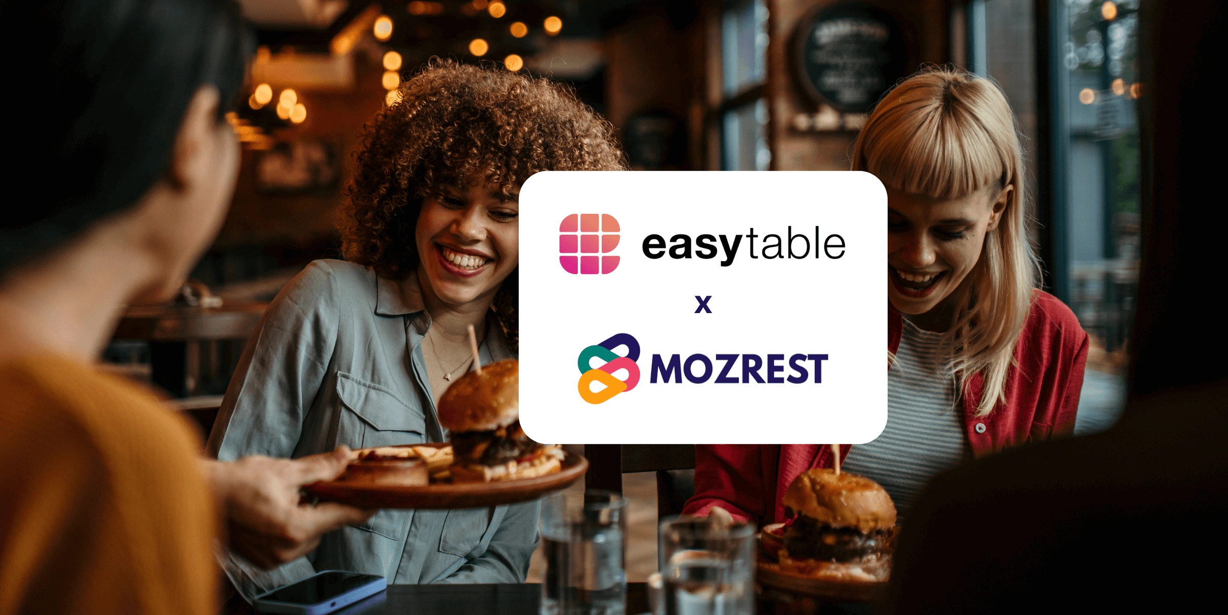 Mozrest - Solutions for Booking Channels - Group of friends seating at a table in a restaurant searching for a their next place to eat on their mobile phone