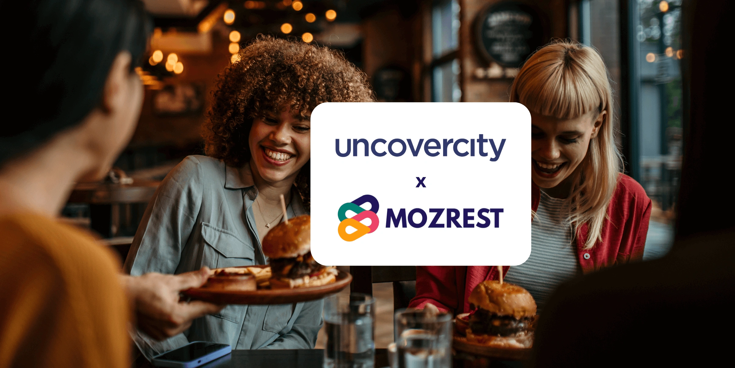 Mozrest - Solutions for Booking Channels - Group of friends seating at a table in a restaurant searching for a their next place to eat on their mobile phone