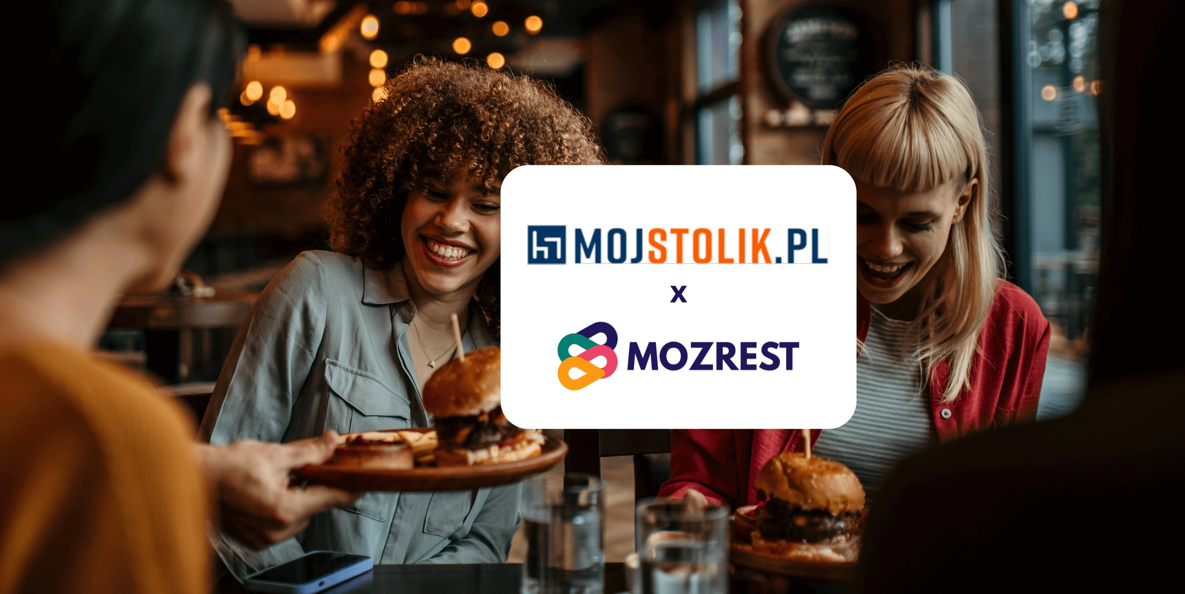 Mozrest - Solutions for Booking Channels - Group of friends seating at a table in a restaurant searching for a their next place to eat on their mobile phone