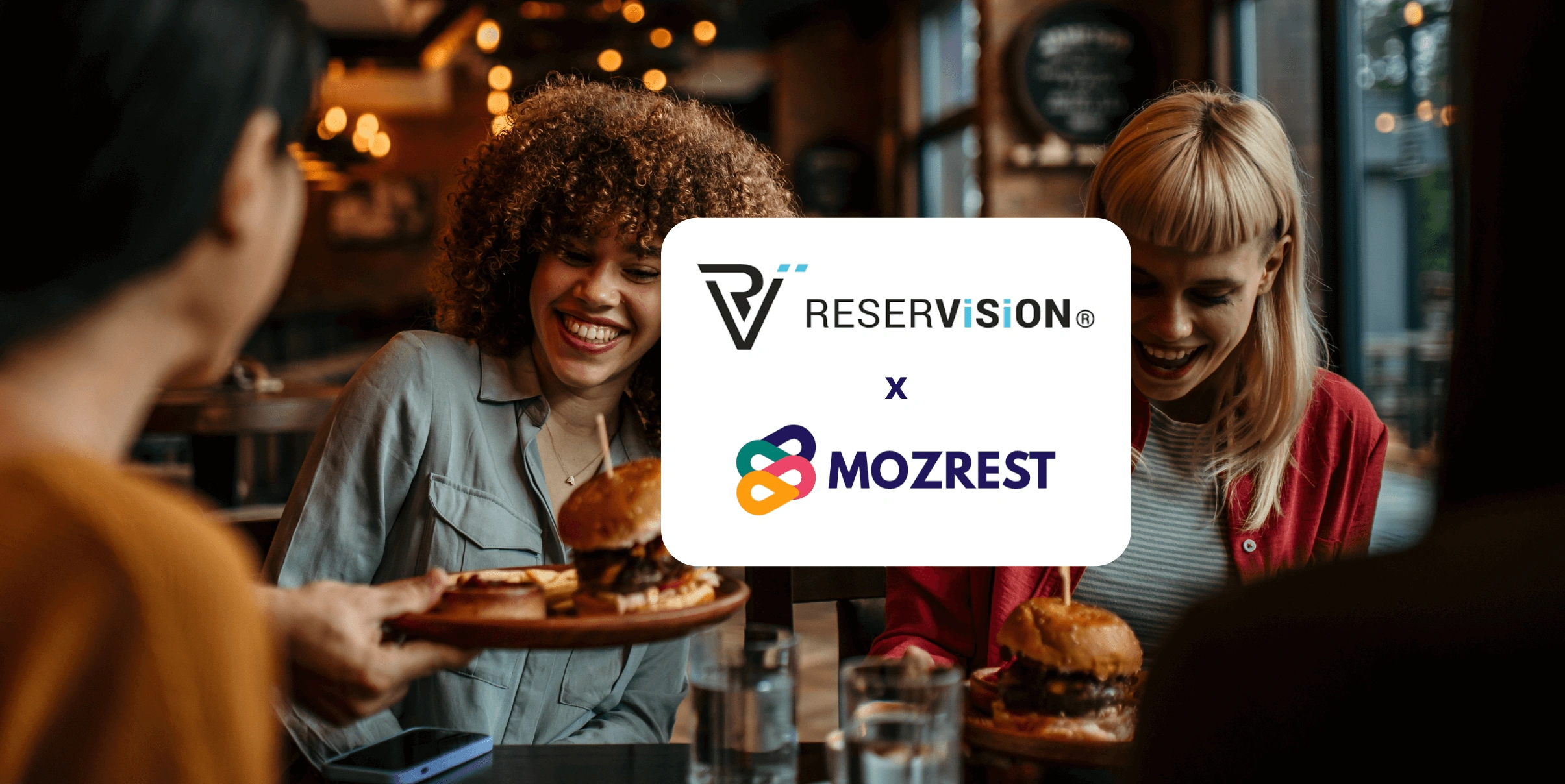 Mozrest - Solutions for Booking Channels - Group of friends seating at a table in a restaurant searching for a their next place to eat on their mobile phone
