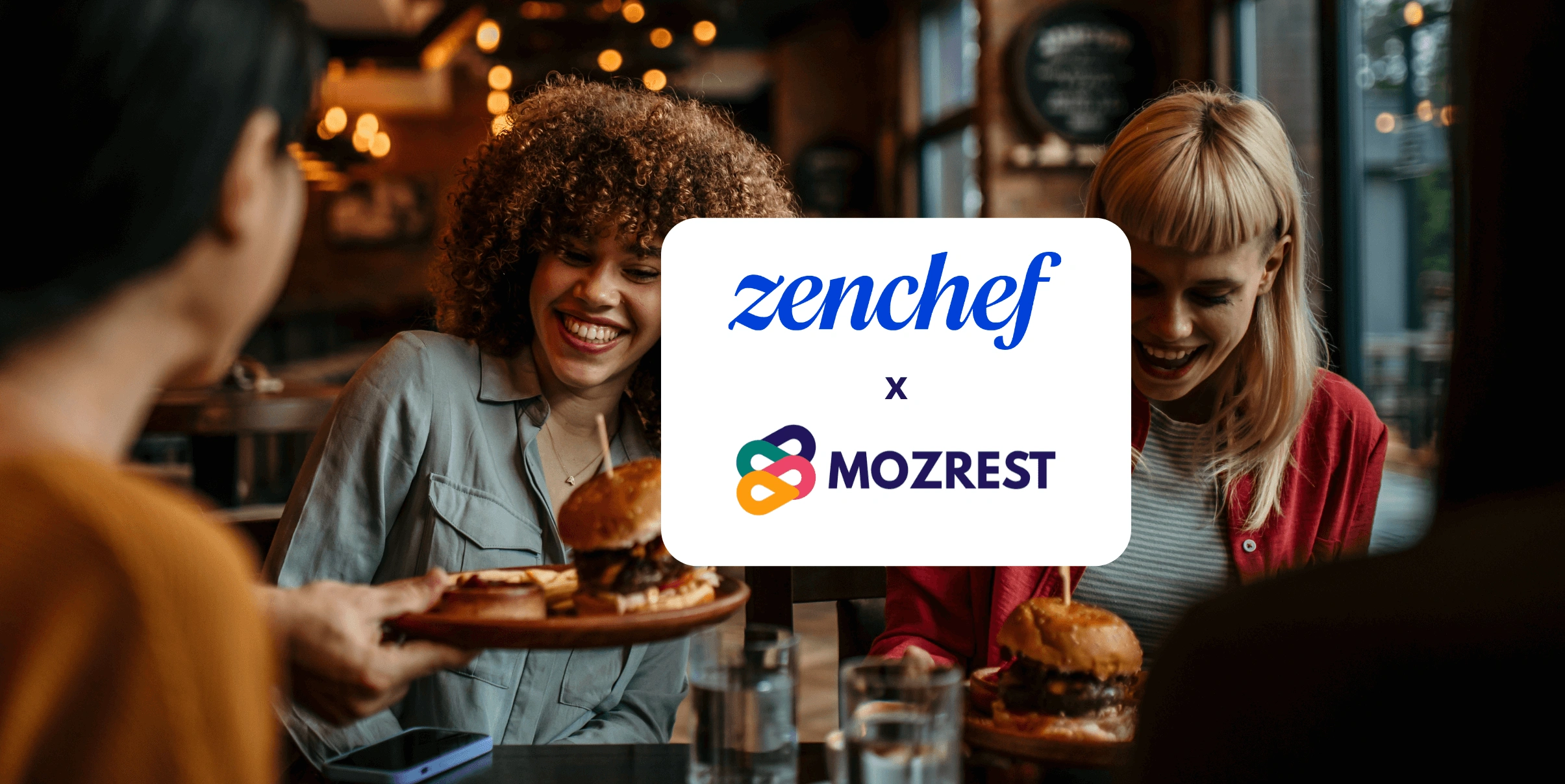 Mozrest - Solutions for Booking Channels - Group of friends seating at a table in a restaurant searching for a their next place to eat on their mobile phone