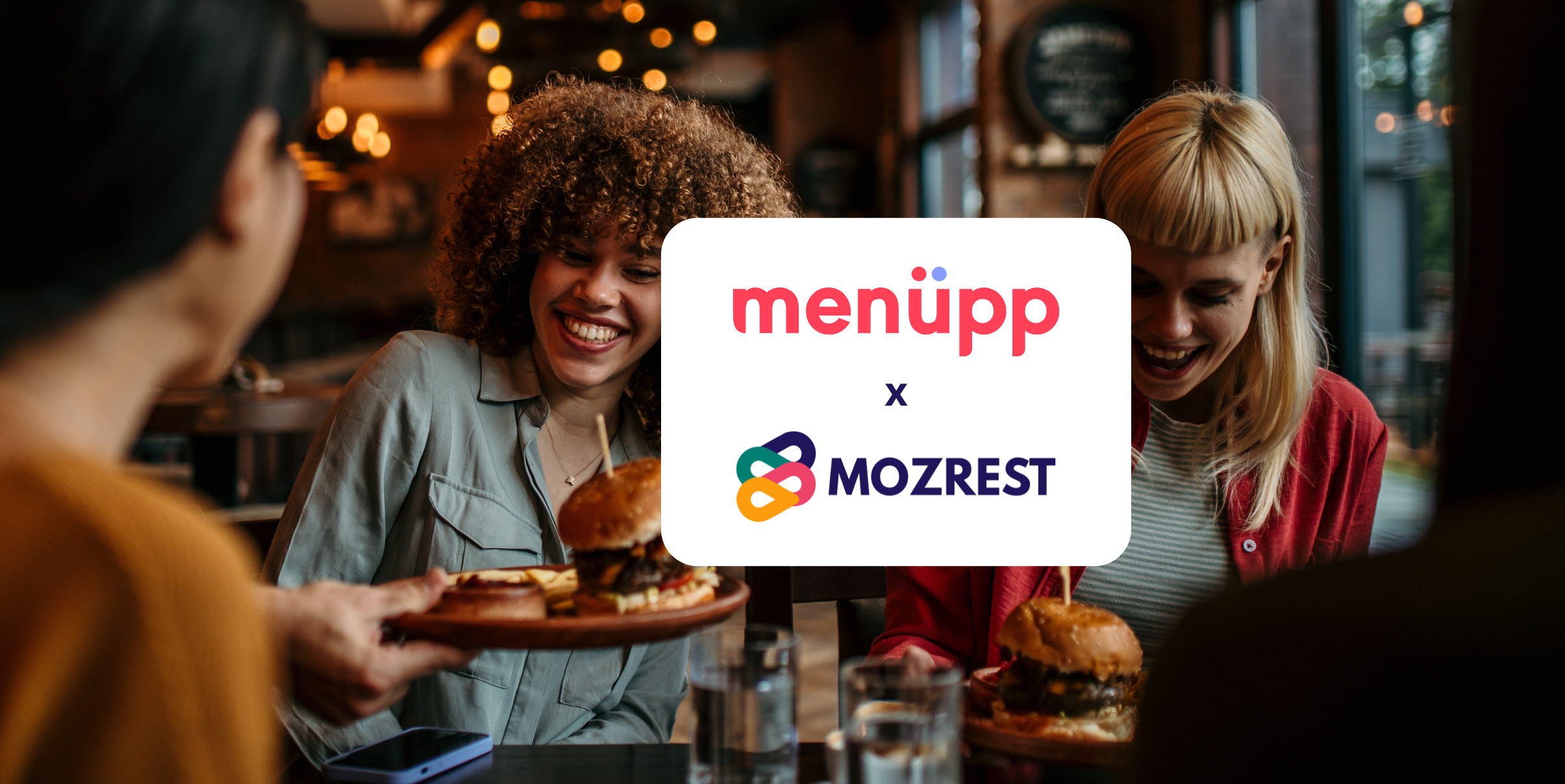Mozrest - Solutions for Booking Channels - Group of friends seating at a table in a restaurant searching for a their next place to eat on their mobile phone