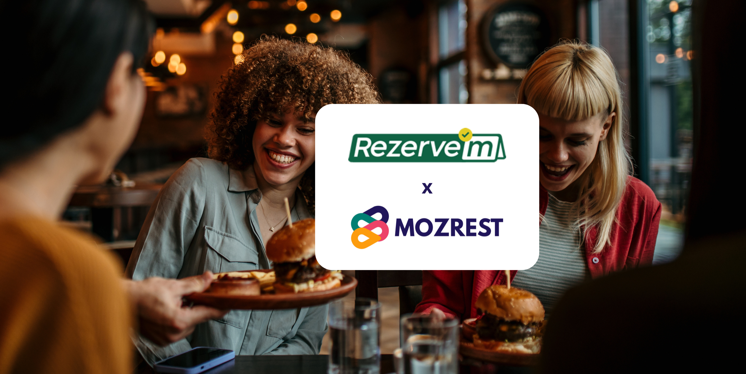 Mozrest - Solutions for Booking Channels - Group of friends seating at a table in a restaurant searching for a their next place to eat on their mobile phone