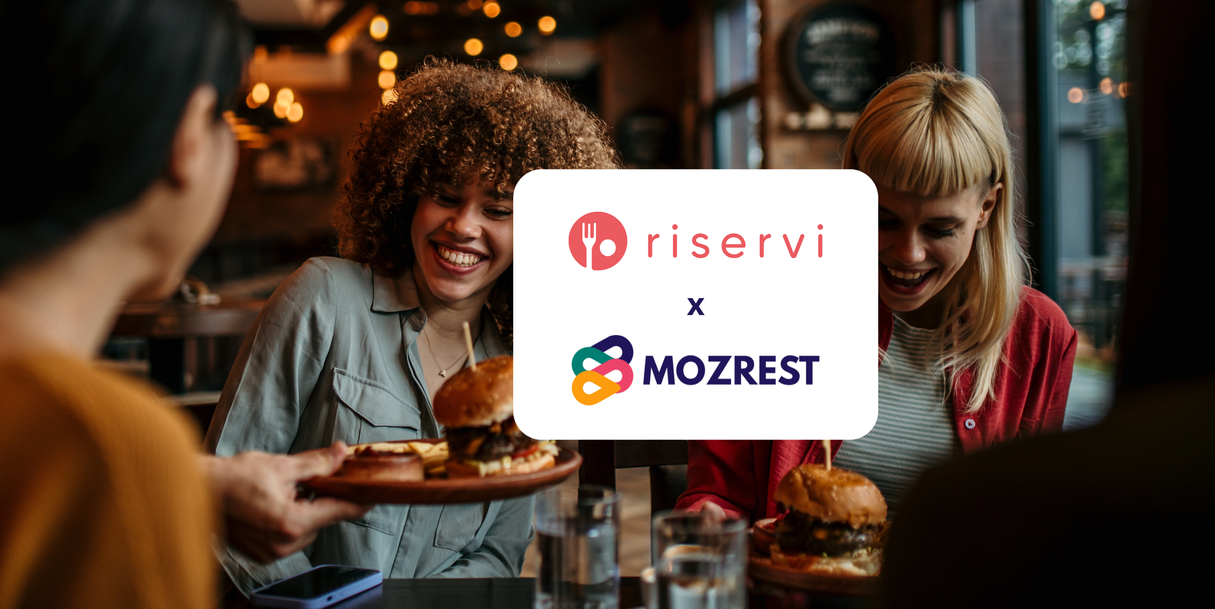 Mozrest - Solutions for Booking Channels - Group of friends seating at a table in a restaurant searching for a their next place to eat on their mobile phone